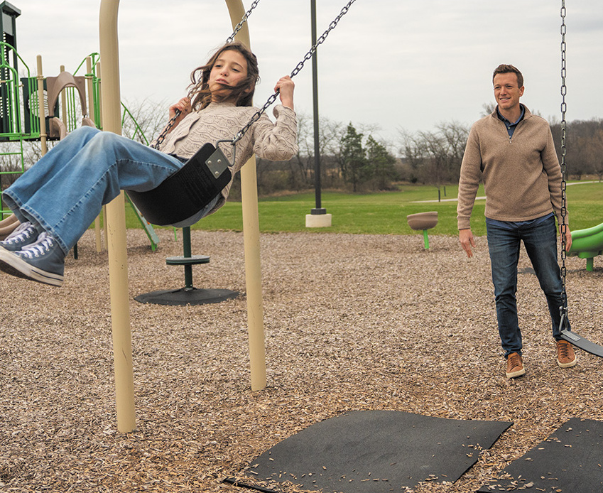 Blake Fiechter with his daughter as she swings on a swing set